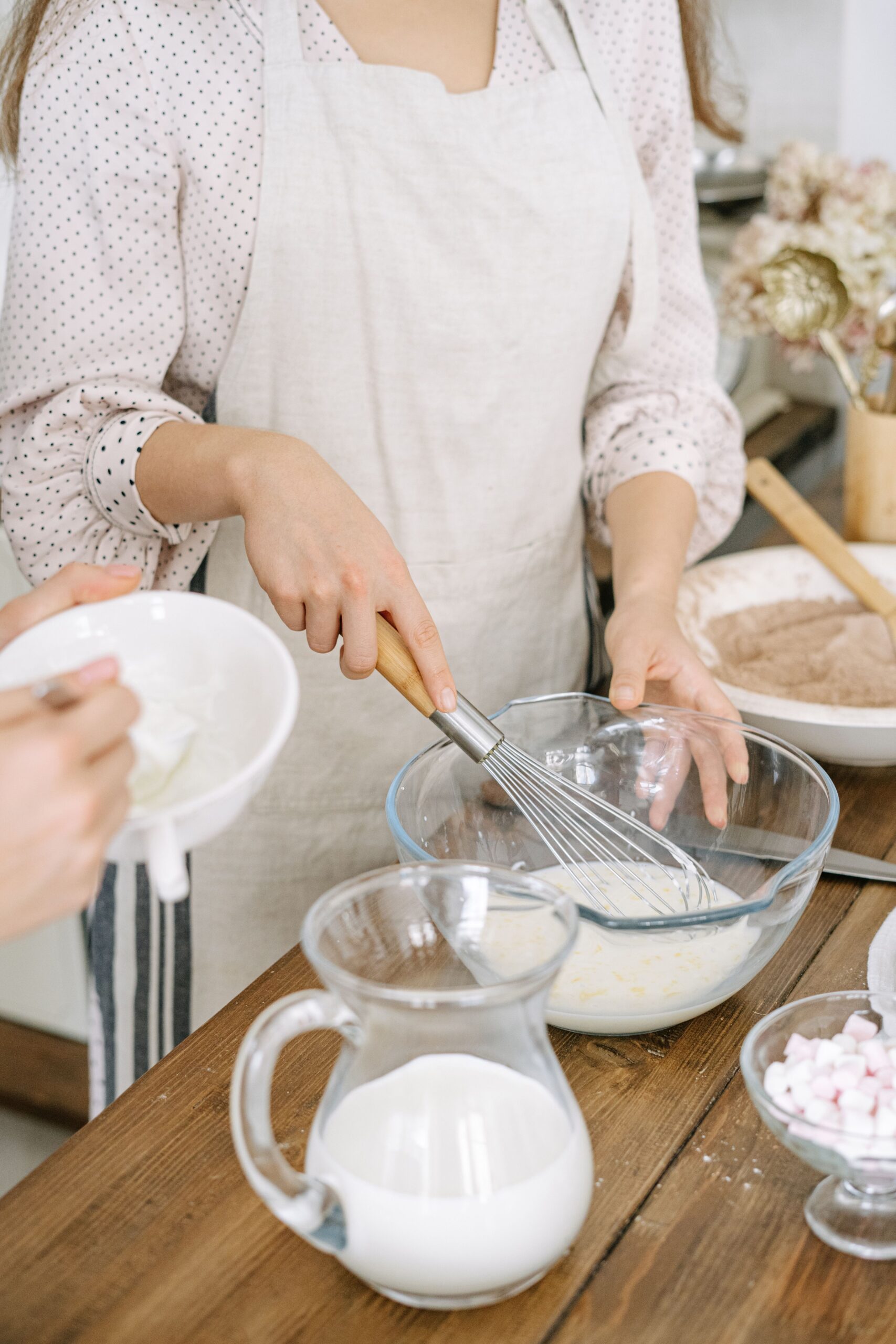 Hands mixing batter in a bowl beside a pitcher of milk