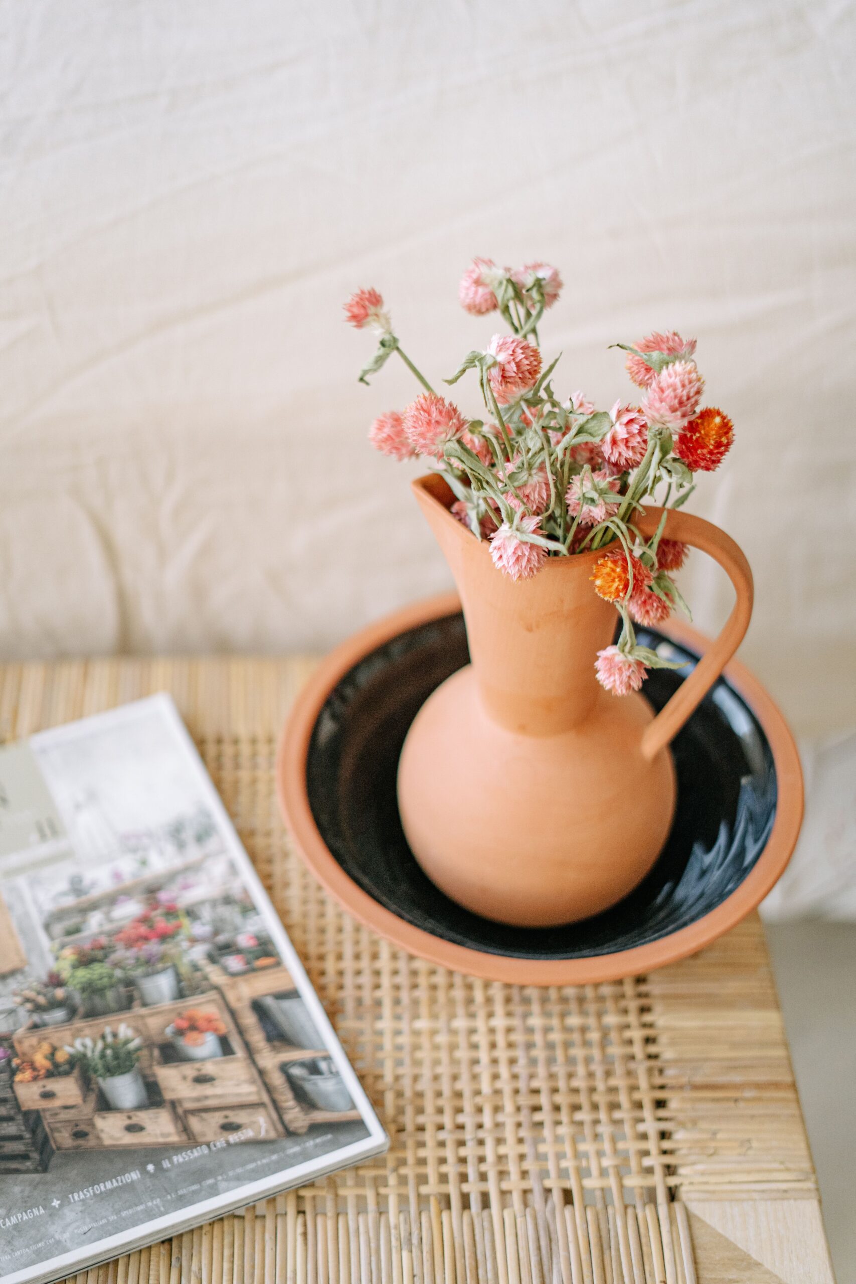 Terracotta pitcher with flowers on a woven mat